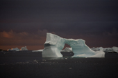 Iceberg with an ice arch grounded in Marguerite Bay. Sunset colours the clouds and the sea Antarctica