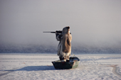 Louis Tepardjuk, an Inuk stands in floe edge boat at the ice edge, & aims his rifle, while hunting. Igloolik, Nunavut, Canada. 1990