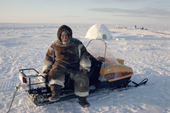 Inuk, Tatigat, in caribou furs sits on his snowcooter near igloo he has built. Igloolik, Nunavut, Canada. 1993