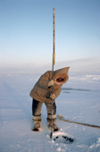 Aipilik, an Inuit hunter uses an ice chisel to make a hole in sea ice for fishing. Igloolik, Nunavut, Canada. 1993