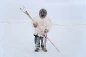 Aipilik, an Inuit hunter, in fox furs with Kakivak (Inuit fish spear) & fish. Igloolik, Nunavut, Canada. 1993