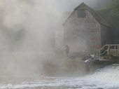Two Coarse Fishermen fishing at the weir by Sturminster Newton Watermill on a foggy morning. Dorset.