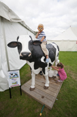 Girl tries to milk a fake cow while a boy rides on it. Sturminster Newton Cheese Festival. Dorset. England