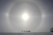 Sun halo and Parhelia (sun dogs) over the Ceremonial South Pole. Part of US Amundsen-Scott South Pole Research station to the right.