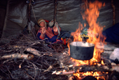 Sami herder, Johan warms himself by the fire in his tent during migration. Kautokeino, North Norway. 1985