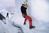 Ice climber practices a traverse on an overhang, watched by associates. Alaska