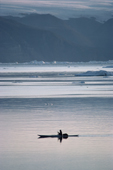 An Inuit hunter paddles his kayak in the calm summer waters of Inglefield Bay. Northwest Greenland. 1980
