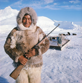 Kigutikak Duneq in fur clothing. He carries a rifle his dogs are behind him. Qaanaaq. Northwest Greenland. (1971)