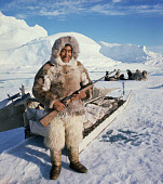 Kigutikak Duneq in fur clothing. He carries a rifle his dog team are behind him. Qaanaaq. Northwest Greenland. (1971)
