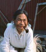 Sinarujuk Sadorana, an Inuit woman with few teeth smoking a pipe, sitting by her house. Qaanaaq, Northwest Greenland. (1971)