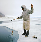 Inuit elder, Masautsiak Eipe fishing for sculpin through a lead in the sea ice. Qaanaaq. Northwest Greenland. (1971)