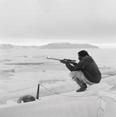 Inuit hunter, Kigutikaq Duneq, waits with his rifle for a seal to surface at the floe edge. Qaanaaq. Thule, Northwest Greenland. 1971
