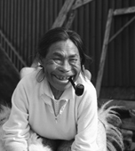 Sinarujuk Sadorana, an Inuit woman with few teeth smoking a pipe, sitting by her house. Qaanaaq, Northwest Greenland. 1971