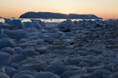 The sun setting behind Herbert island highlights pieces of glacial ice on the shore of Inglefield Bay. Northwest Greenland. 2008