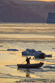 At sunset, an Inuit hunter manoevres his boat through newly formed sea ice in autumn. Inglefield Bay. Qaanaaq, Northwest Greenland. 2008