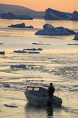 At sunset, an Inuit drives his boat through newly formed sea ice in Inglefield Bay. Qaanaaq, Northwest Greenland. 2008