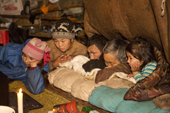 A Chukchi family watching a movie on a notebook computer by candlelight inside a Yaranga (traditional tent) at a reindeer herder's camp. Iultinsky District, Chukotka, Siberia, Russia.