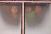 Lena Potapova & her sisters Varya & Tanya look through a window at their home in Verkhoyansk, Yakutia, Republic of Sakha. (1999)