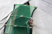 Stella Piak, A Forest Nenets girl, peers through the mosquito net at the entrance to her family's tent. Purovsky Region, Yamal, Western Siberia, Russia