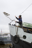 A deck hand throws a rope from a fishing boat as it prepares to dock at the quayside at Aksarka on the River Ob. Yamal, Western Siberia, Russia