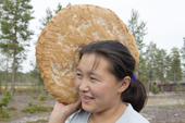 Lena Kuboleva, a young Selkup woman, holding a loaf of traditional Selkup bread she has baked in hot sand, at her family's summer camp in the forest. Krasnoselkup, Yamal, Western Siberia, Russia.